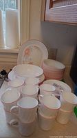 Corelle dishes including mugs, bowls, plates, and platter with pink floral design stacked on kitchen counter