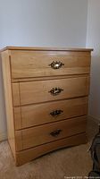 Front view of light wood laminate dresser showing four drawers with gold tone handles.