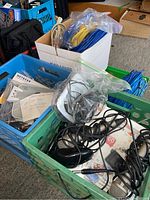 Two plastic crates and two cardboard bins filled with various electronic items including network cables, computer mice, and a Netgear wireless adapter in original packaging.