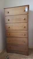 Front view of a tall wood six-drawer dresser with wood knobs and visible label on top drawer corner.
