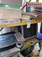 Two metal shelves with paper stacks, PaperPort software box, IBM paper, DVD spindle and iMac base