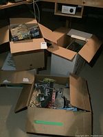 Three cardboard boxes containing various model train scene supplies, including buildings, greenery, and hardware.