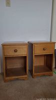 Pair of light wood night stands viewed from front showing single drawer with wood knob and open shelf below on a beige carpet.
