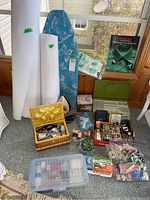 Overall view of sewing supplies including batting, ironing board, sewing box, thread organizer and accessories grouped on floor