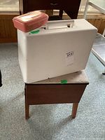 Kenmore sewing machine in white plastic carry case sitting on wooden stool.
