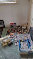 Wide view showing the cream-colored Kenmore sewing machine on left and large tote filled with assorted sewing notions on right. Various small sewing items scattered on carpet in front of tote.