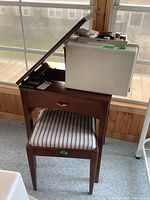 Wood-finish sewing table with hinged top open, upholstered stool and white plastic carry case