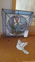 Photo showing orchid stained glass panel with dove and small heart pieces on table.