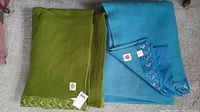 Two blankets, green and blue, both with floral satin edging and wool texture.