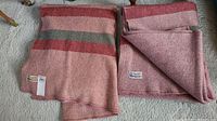 Two folded wool blankets showing mauve color with red and green stripes, lying side by side on carpet.