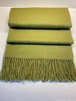 Folded muted green cashmere throw with visible fringe tassels at one end.