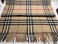 Photo showing pale tea wool throw spread and folded with clear view of black, red, and cream check pattern and fringed ends
