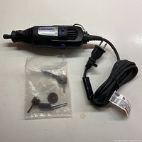 Full view of black Dremel 1001 rotary tool with power cord and plug, along with plastic bag of sanding attachments.