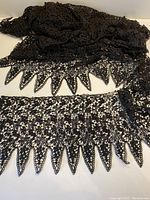 The full length of the black lace trim showing its width and scalloped edges gathered together.