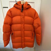 Front view of bright tangerine mid-length puffer coat with hood on a hanger.