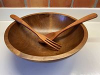 Salad bowl with fork and spoon resting inside, showing wood grain and smooth finish
