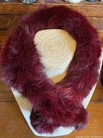 Front view of burgundy fur scarf arranged circularly on display stand showing plush texture and material quality.