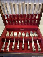 Full 10-place setting flatware arranged in wooden display box with burgundy velvet slots.