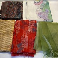 Overview of five silk scarves folded and displayed, showing various colors and textures.