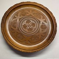 Full view of the circular wooden plate showing the entire carved design and scalloped edges.