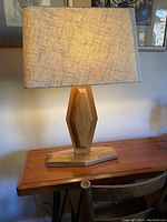 Wooden geometric diamond-shaped lamp with fabric shade on wooden table surface, showing the front and side views