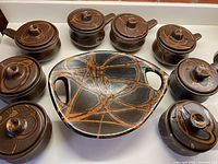 Photo displaying eight ceramic French onion soup bowls with lids in dark milk chocolate glaze with cinnamon swirls arranged around a large matching ceramic bread plate.