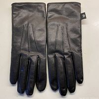Front view of pair of black leather gloves with three stitched lines detail on back, showing smooth leather texture and small tab on wrist.