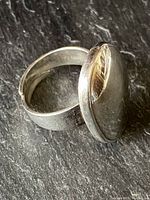 Close-up angled view showing large oval silver disc and portion of plain silver band with adjustable gap underneath.