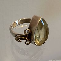 Close-up photo showing the pear-shaped pale semi-precious stone bezel set in sterling silver with swirling side loops, with visible 925 stamp inside the band.