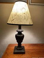 Full view of the lit table lamp showing the textured beige and brown lamp shade and dark ornamental base.
