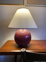 Full view of the vintage cherry red bubble gum lamp on a wooden table, showing the spherical ceramic base and white lampshade.