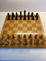 Full view of the wooden folding chessboard with all chess pieces set up in starting position; chessboard with alternating wood grain squares.