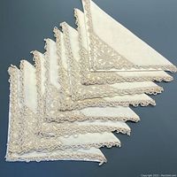 Set of 8 pale cream linen napkins arranged fanned out showing lace tatting edges and corners