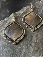 Two vintage sterling silver earrings with mother of pearl discs and marcasite stone accents placed on dark stone surface.