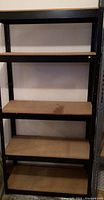 Narrow shelving unit front view showing five particle board shelves and black metal frame