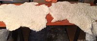 Two lambskin rugs displayed on a wooden surface from the wool side, showing off-white curly wool texture and irregular natural edges.