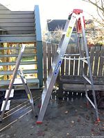 Werner 6 ft aluminum ladder set up in A-frame position outdoors, showing red handle and orange foot caps.