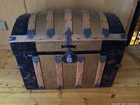 Front view of the antique wooden dome-top trunk showing wood slats and dark metal bands with locking clasp.
