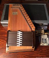 Front view of Appalachian wooden autoharp with protective case in background and accessories to the side.
