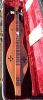 Full view of dulcimer inside red plush-lined hard case with accessories visible