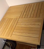 Top view of the square blonde oak folding table showing the slatted wood pattern divided into four quadrants.