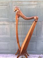 Full-height view of harp standing against a garage door showing overall shape, pillar, neck, soundbox and legs.