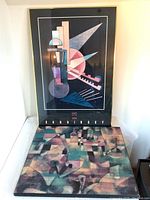 Kandinsky framed print in black and gold frame with bold geometric shapes, and Paul Klee print on wood panel with pastel abstract composition underneath.