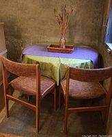 Two teak frame chairs positioned in front of the dining table covered with tablecloths
