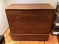 Front view of mid-century modern teak dresser with 5 drawers and recessed handles.