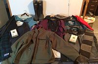 Full overview of jackets, scarves, boots and handkerchiefs on bed showing lot contents