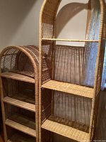 Photo showing both natural rattan shelf units standing side-by-side, tall unit on the right and shorter unit on the left, highlighting the material and design.