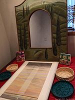 Full view of hand painted archway mirror with landscape background, print, baskets, mini canvases on table against wall.