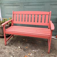 Front view of red wooden outdoor bench showing slatted seat, backrest, and armrests, placed on concrete surface against a green door background.