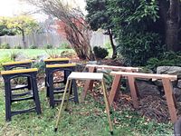 View showing 2 wooden sawhorses, 4 black and yellow plastic sawhorses, and Welt Safe-Lock project stand in grass outside